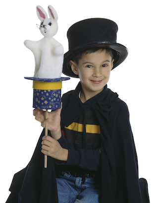 A little boy dressed in a top hat and cape making a felt rabbit emerge from a papier-mâché hat.